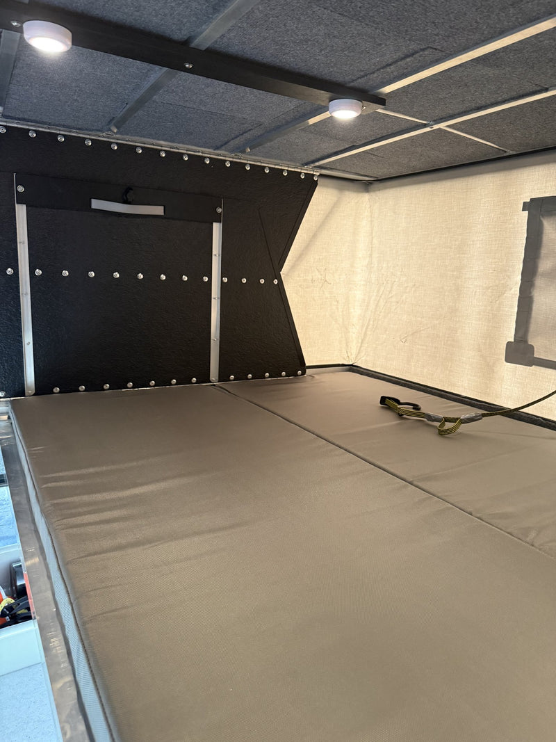 Interior view of the sleeping area with the north-south foam mattress platforms laid out edge to edge, the insulated canvas side wall with a window cover, LED puck lights overhead and the black insulated front wall — photo 4