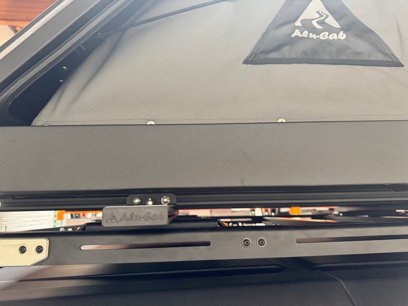 Detail of the Alu-Cab branded aluminum mounting bracket and rail hardware on the underside of the Gen 3-R tent, with the canvas and shell edge above — photo 7