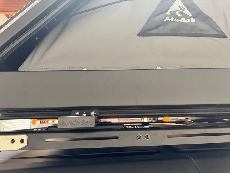 Detail of the Alu-Cab branded aluminum mounting bracket and rail hardware on the underside of the Gen 3-R tent, with the canvas and shell edge above — photo 7