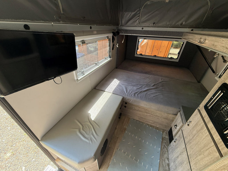 Interior from above showing the 24-inch TV, bench seat and the king-size main bed under the pop-up roof — photo 12
