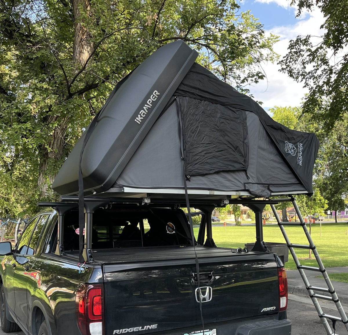 iKamper Skycamp 3.0 Mini rooftop tent opened on a black Honda Ridgeline bed rack, hardshell lid raised and telescoping ladder deployed to the ground