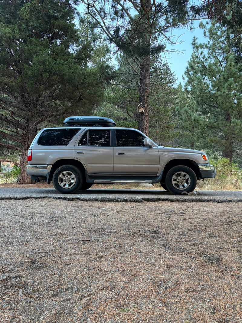 2002 Toyota 4Runner 2WD in silver, driver-side profile, with Garvee rooftop cargo box, parked in a pine forest campsite — photo 1