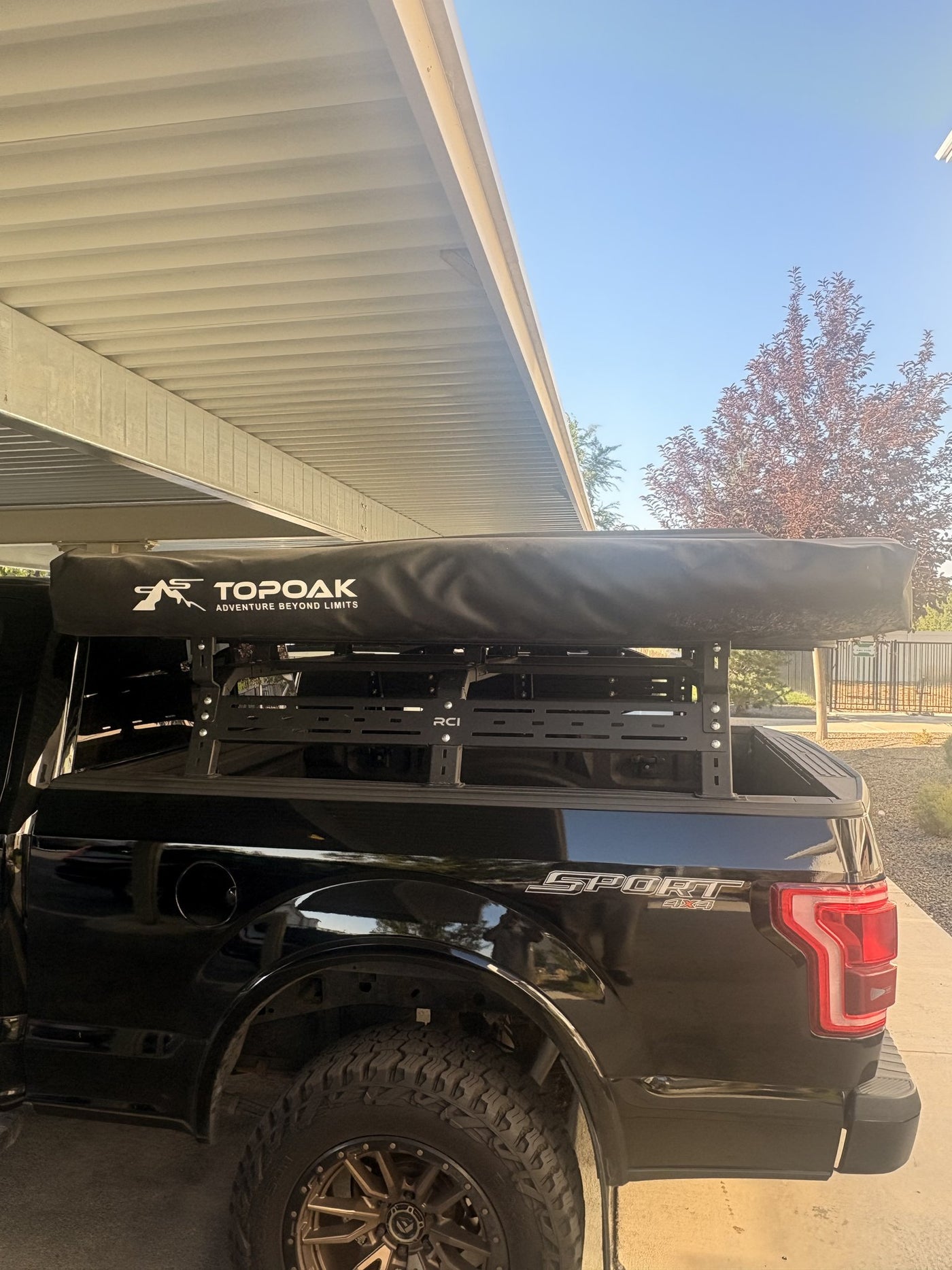 Driver-side view of the Topoak 180-degree awning in its black cover running along the top of the RCI bed rack, showing the slotted rack side panels over the F-150 bed — photo 3