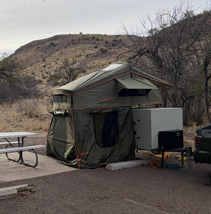The trailer set up at a desert campsite with the Roam Vagabond rooftop tent deployed and its full annex room zipped on to the ground, hitched beside a picnic table with hills behind — photo 2