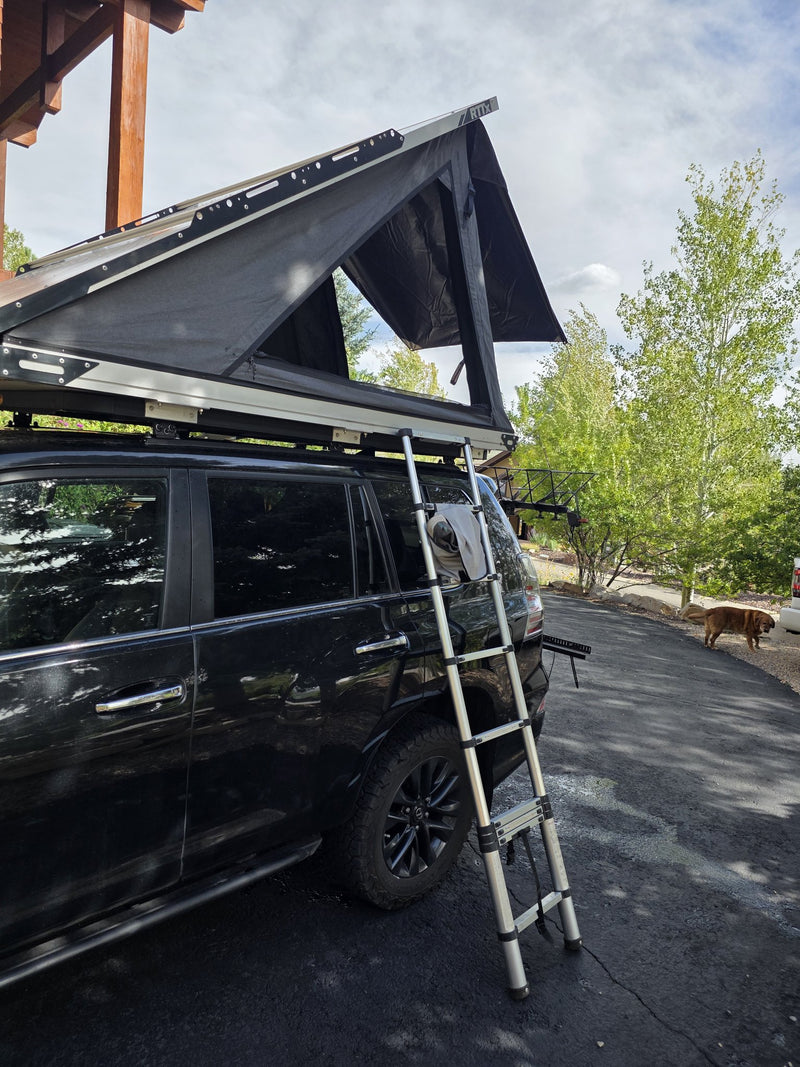 Side view of the deployed Terrapod RTTx XL with the telescoping ladder leaning against the vehicle, showing the open tent canopy and the full length of the hard shell — photo 10