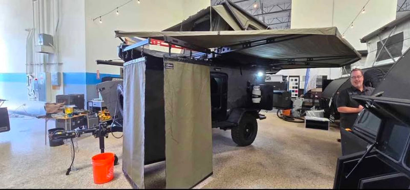 Bush Company Outpost shower enclosure set up alongside the XPedition Voyager Sky XE indoors, hanging from the awning rail with the awning extended overhead — photo 17