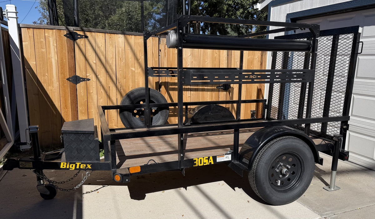 Driver-side full profile of the black 2023 Big Tex SA-30 single-axle utility trailer on a concrete driveway, showing the custom black steel overhead rack with slotted RCI crossbars, the wood-plank deck, diamond-plate tongue storage box, mounted spare tire and the yellow 30SA model decal on the fender