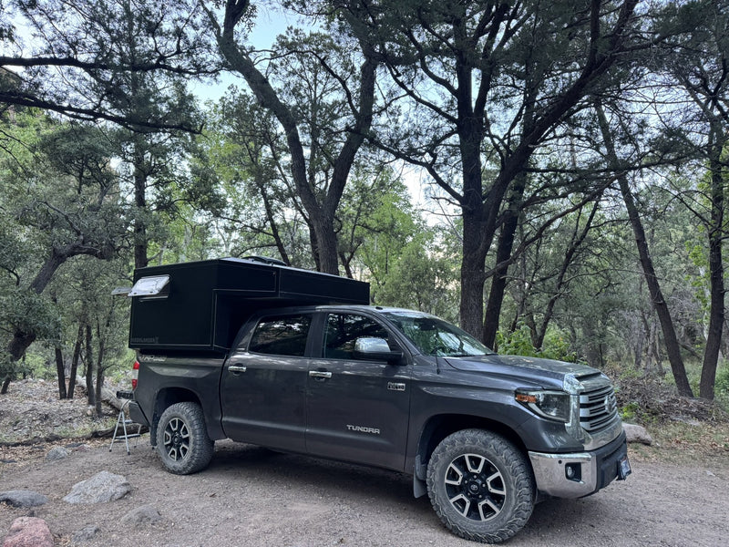 Black Radica Moonlander X hard-shell truck camper mounted on a Toyota Tundra at a wooded campsite — photo 1