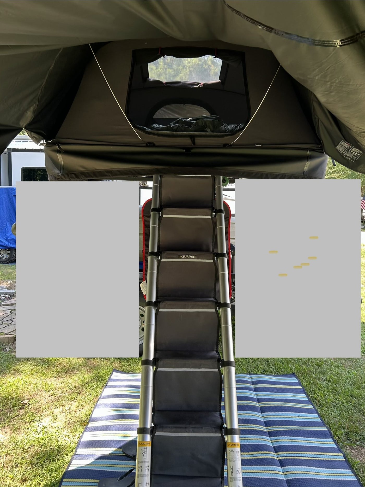 Looking up at the open tent from ground level with the iKamper telescoping ladder extended down to a camp mat, fabric steps fitted over the rungs and the tent floor and door above — photo 6