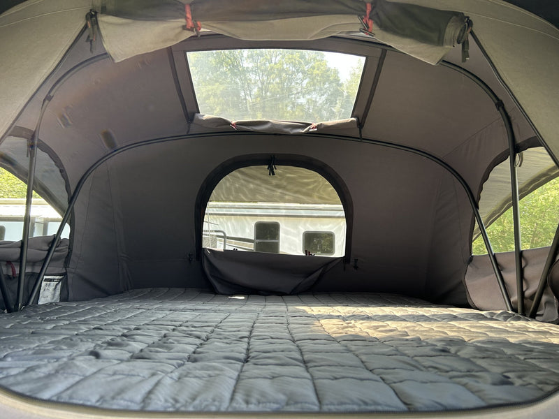 Interior of the rooftop tent looking out through the arched doorway and upper window, showing the quilted mattress, the interior insulation liner and the black support poles — photo 4