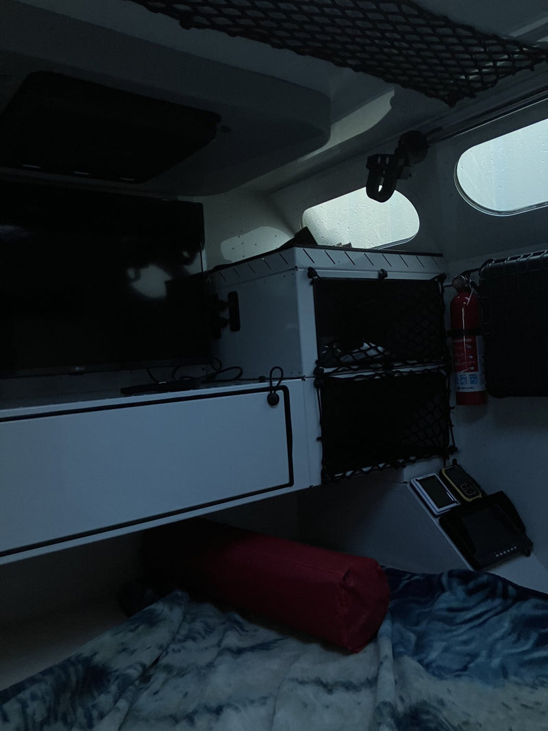 Interior sleeping area of the 2023 Mammoth Overland ELE: bedding on the platform, overhead cargo nets, a fire extinguisher, a control panel and monitor on the cabinet face, and a storage cabinet along the wall — photo 7