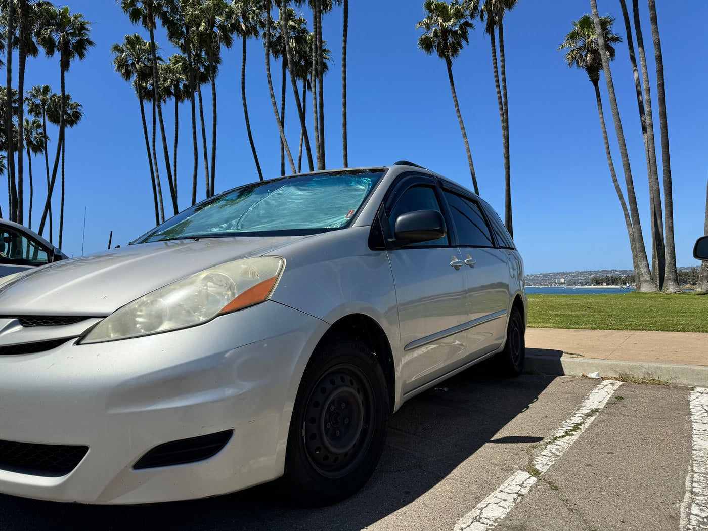 Silver minivan parked on a sunny day near palm trees and ocean. Perfect for family travel; consider an rv rental for group trips. — photo 4