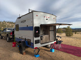 Enjoying nature with this **rv rental**: a SunRay Sport travel trailer with outdoor kitchen, truck, and dog in a scenic, rustic camp.