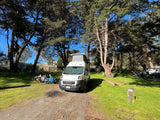 Enjoying the outdoors in an RV rental: A Winnebago campervan with its pop-top extended at a sunny, wooded campsite.