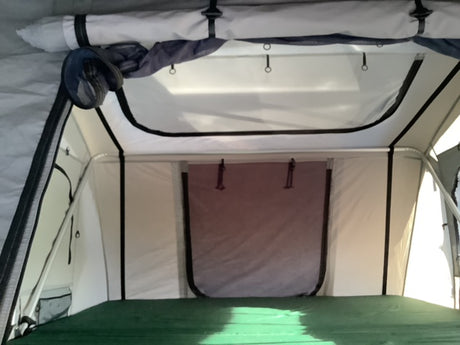 RV rental rooftop tent interior: Bright sleeping area with green mattress & overhead mesh storage. Ideal for camping.