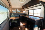 Modern RV rental interior: well-equipped kitchen, comfortable bed, and dinette with snowy landscape views.