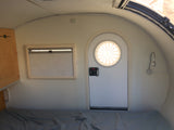 This rv rental interior features a cozy bed, window with blinds, cabinet, and a door with a circular window.
