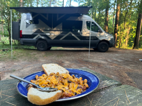 Camping comfort: Cheesy chili mac & bread on a picnic table with our adventure-ready rv rental parked behind.