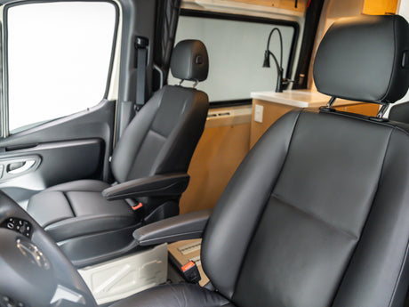 Spacious RV rental front cabin with comfortable black seats and armrests, looking back towards the camper van's kitchen.