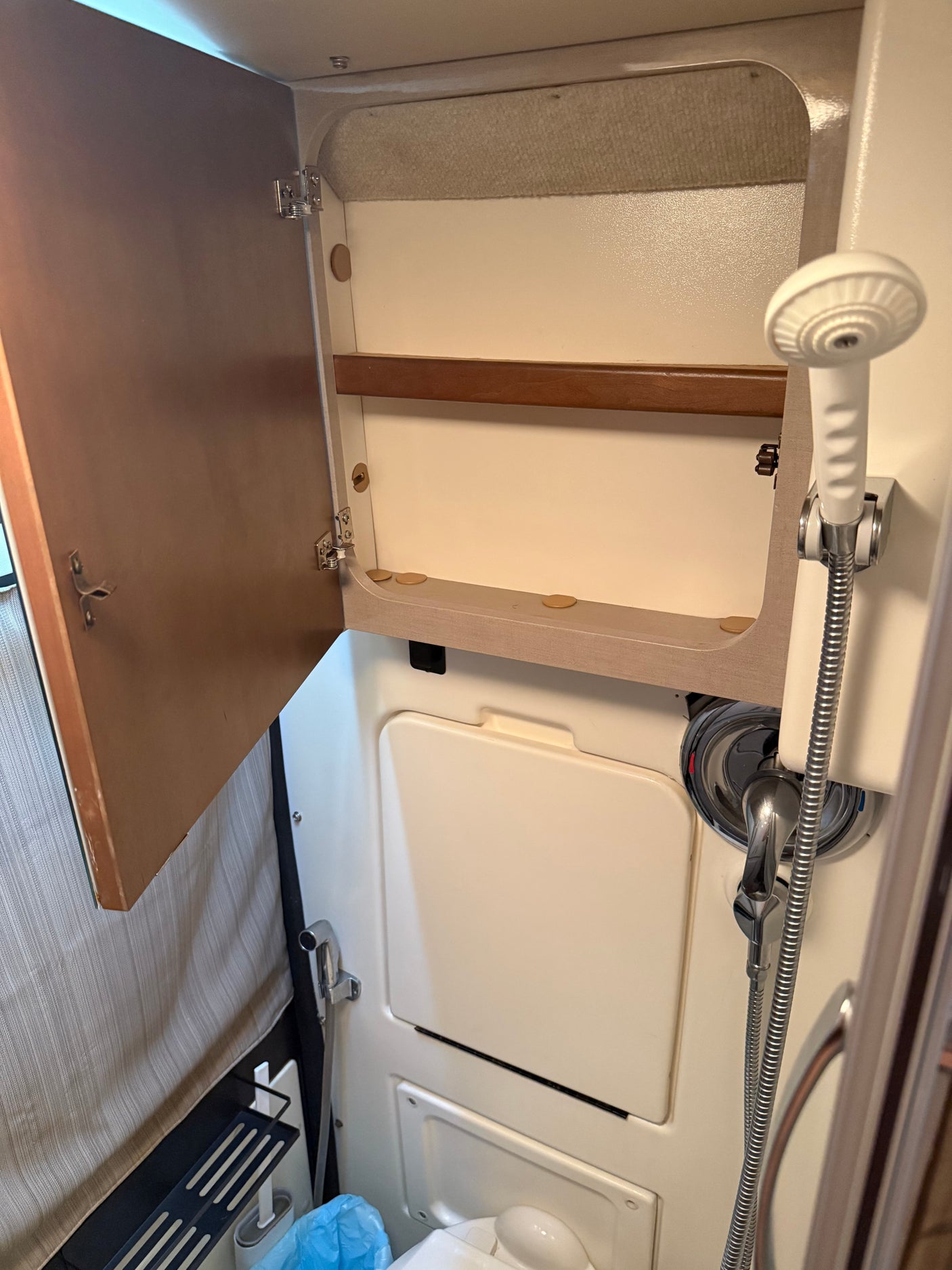 Compact RV rental bathroom with open storage cabinet, handheld shower, and toilet area. Perfect for travel convenience.