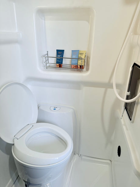 Clean rv rental bathroom featuring a Thetford toilet, shower, and "thanks to nature" toiletries on a wall-mounted shelf.