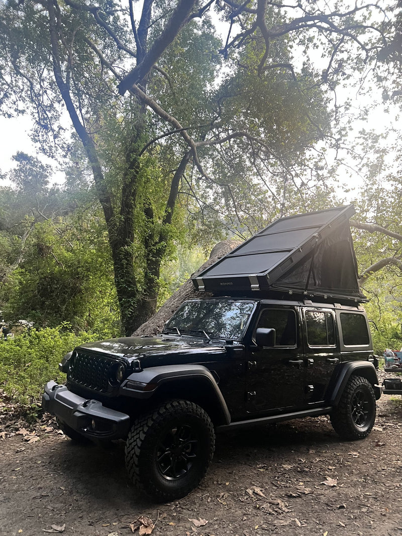Side view of the BDV Duo fully deployed under a large tree, showing the full length of the opened canopy, the zippered window panels and the hardshell base on the rack — photo 3