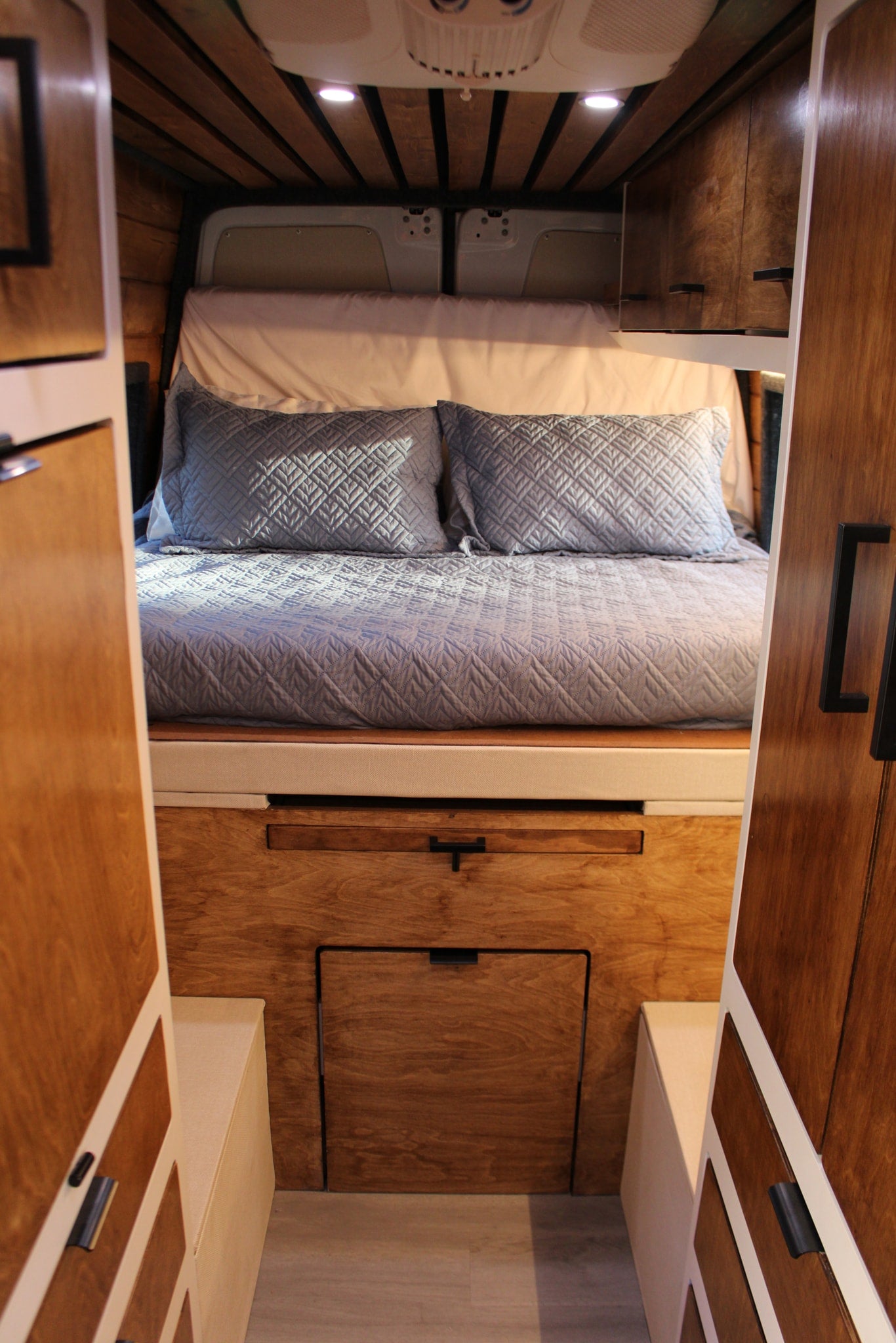 Plush bed in a cozy RV rental, featuring warm wood cabinetry, overhead lighting, and smart storage. — photo 4