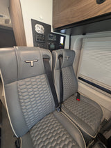 Comfortable grey quilted seats with T-logos, seatbelts, and a full control panel in this RV rental.