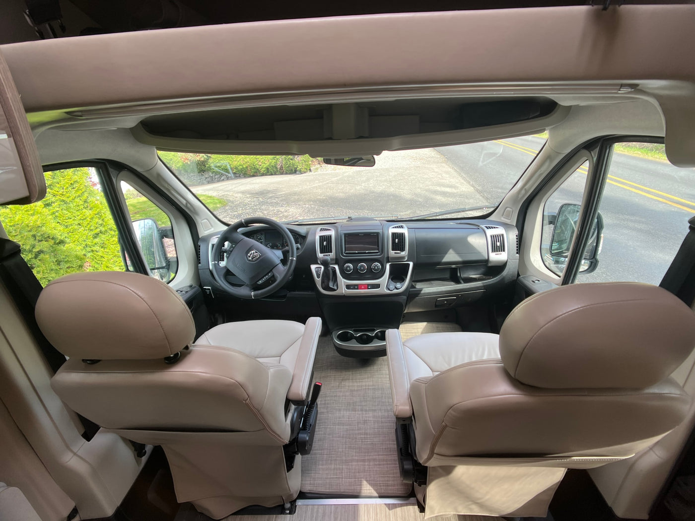 RV rental interior: View from the rear of a bright cab with tan captain's chairs, dashboard, and Ram steering wheel. — photo 13