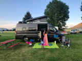 Family preparing camp with their **RV rental**, a gray camper van with pop-top, at a grassy campsite.