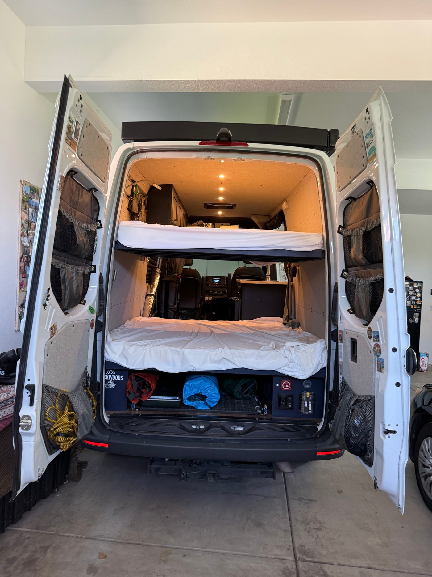 Rear view of a spacious RV rental interior: bunk beds, gear storage, and open rear doors revealing a fully converted van. — photo 11