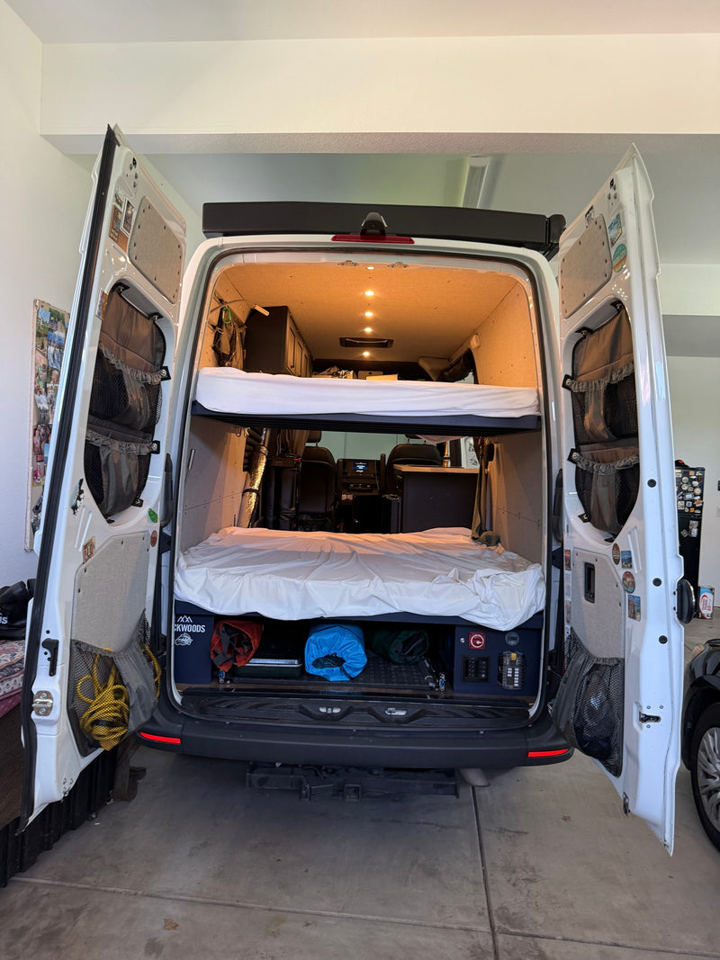 Rear view of a spacious RV rental interior: bunk beds, gear storage, and open rear doors revealing a fully converted van. — photo 11