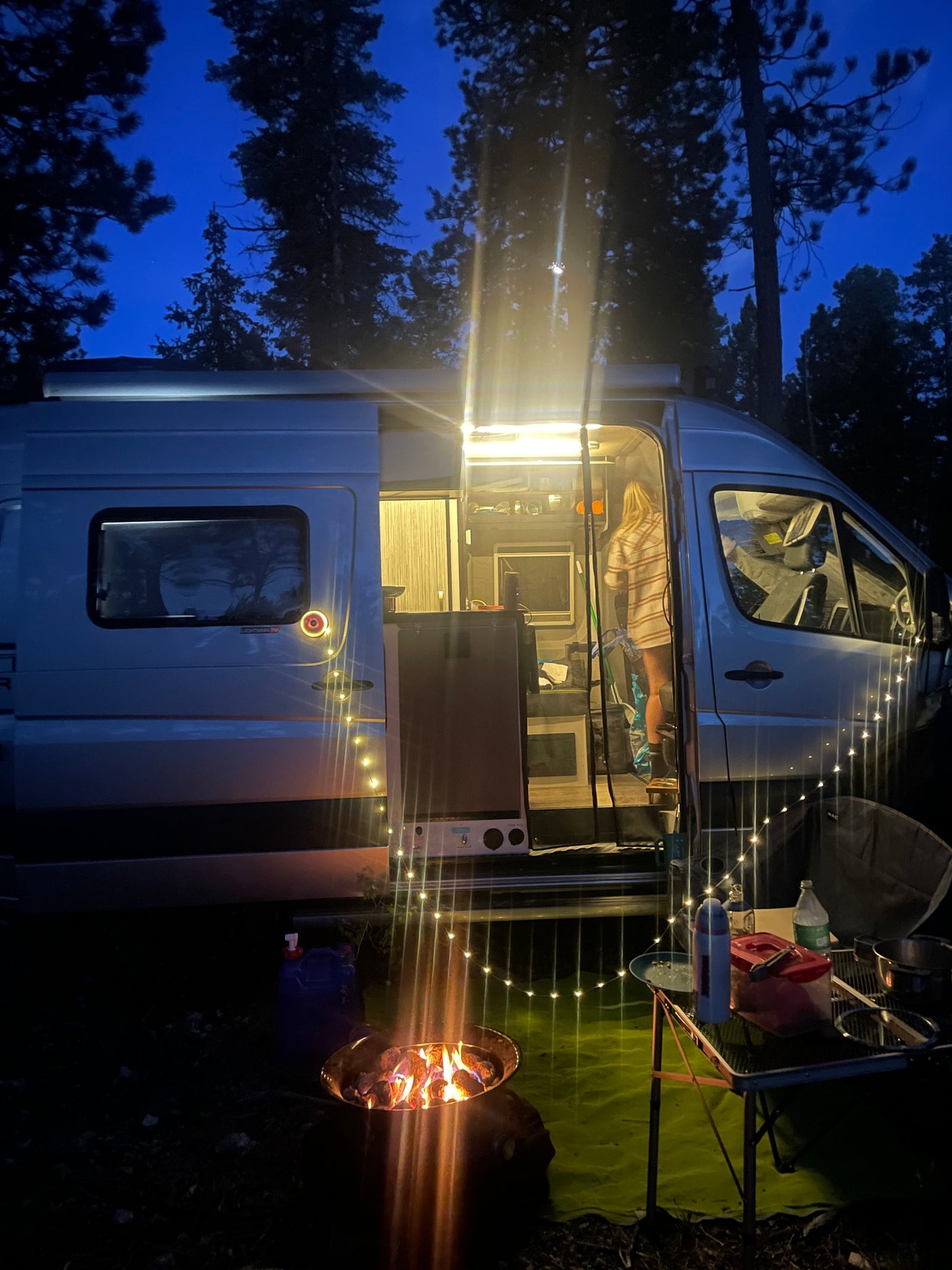 Cozy RV rental setup at night with bright interior lights, string lights, and a warm fire pit. — photo 19