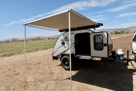A modern Freesold teardrop rv rental with an extended awning, set in a scenic field with distant mountains.