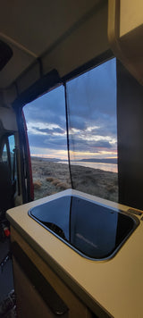 RV rental sunset view: A peaceful evening scene from inside a camper van, featuring a large screen window and kitchen sink.
