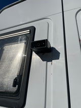 Detail of an **rv rental** side: a mounted black camera/sensor next to a window with a textured interior, showing minor wear.