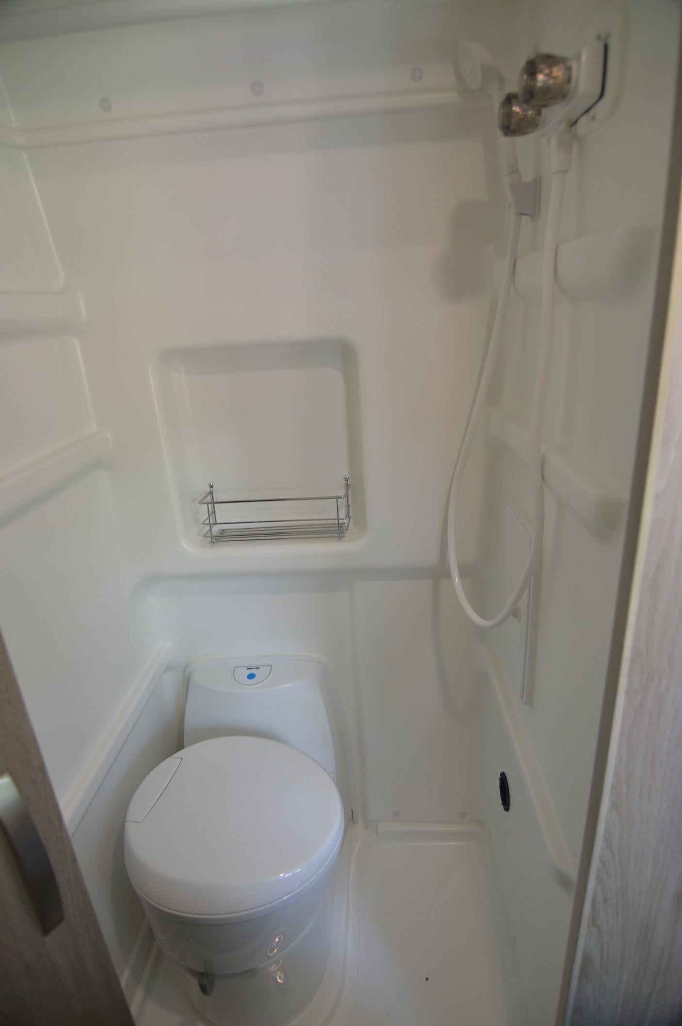 White, compact wet bath in an rv rental, featuring a toilet, shower hose with faucets, and a wire shelf.