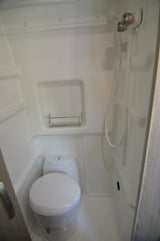 White, compact wet bath in an rv rental, featuring a toilet, shower hose with faucets, and a wire shelf.
