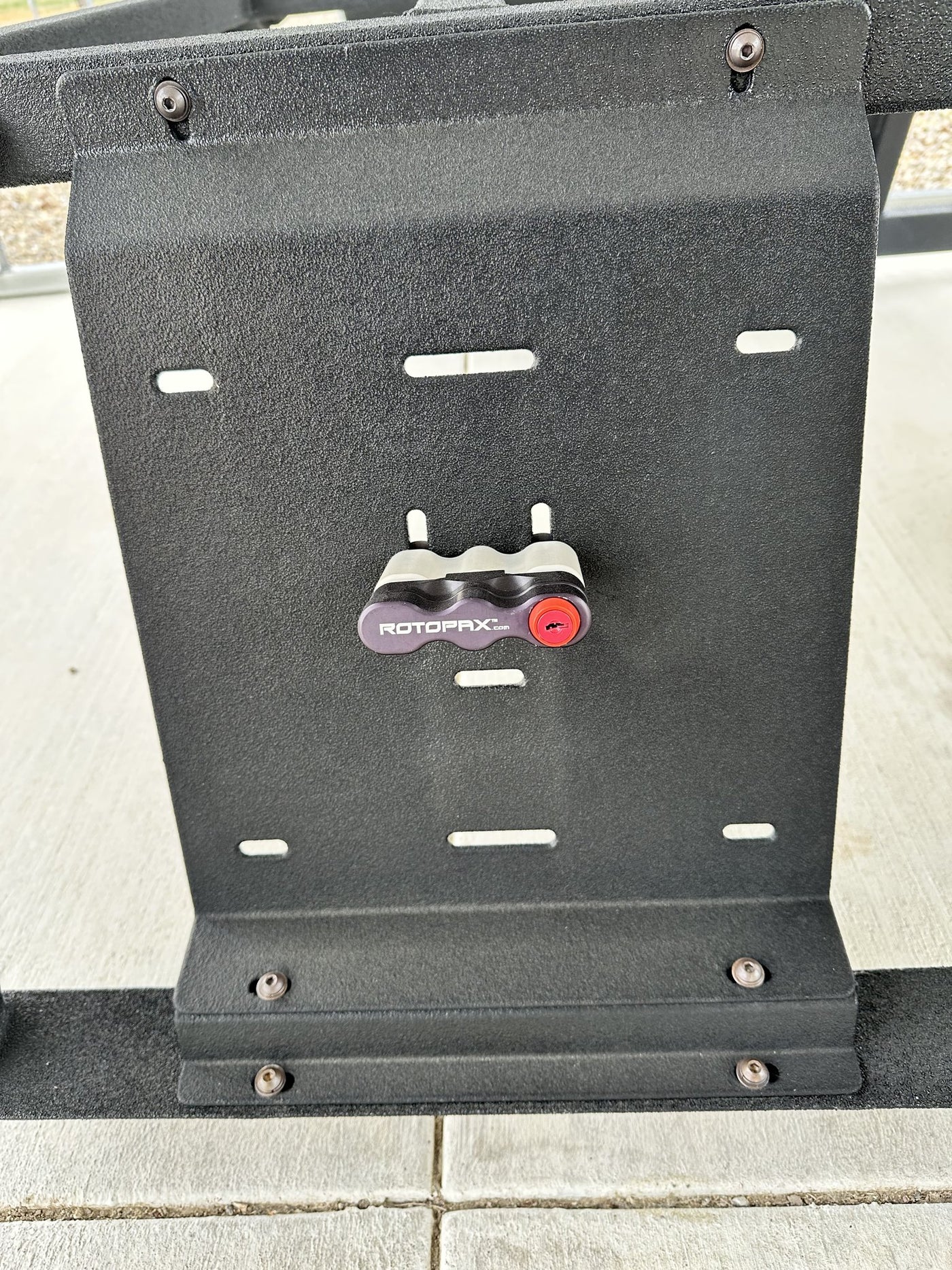 Close view of a universal mounting plate with a Rotopax locking fuel can mount bolted to it, slotted holes for adjustment and stainless hardware in the rhino lined panel — photo 5