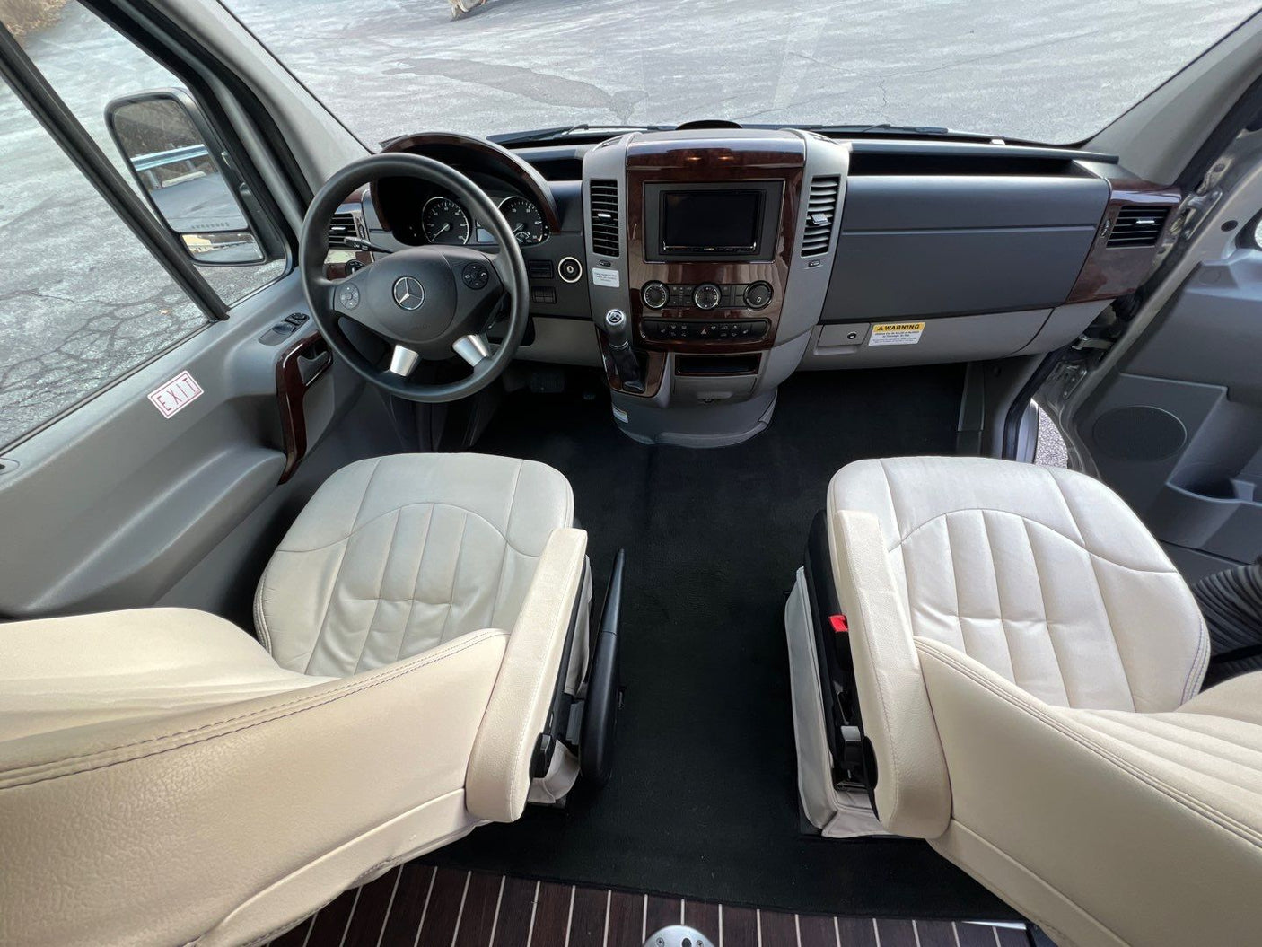 Inside an RV rental: luxurious front cabin with light leather seats, wooden trim dashboard, and steering wheel.