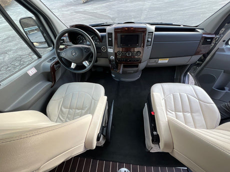 Inside an RV rental: luxurious front cabin with light leather seats, wooden trim dashboard, and steering wheel.