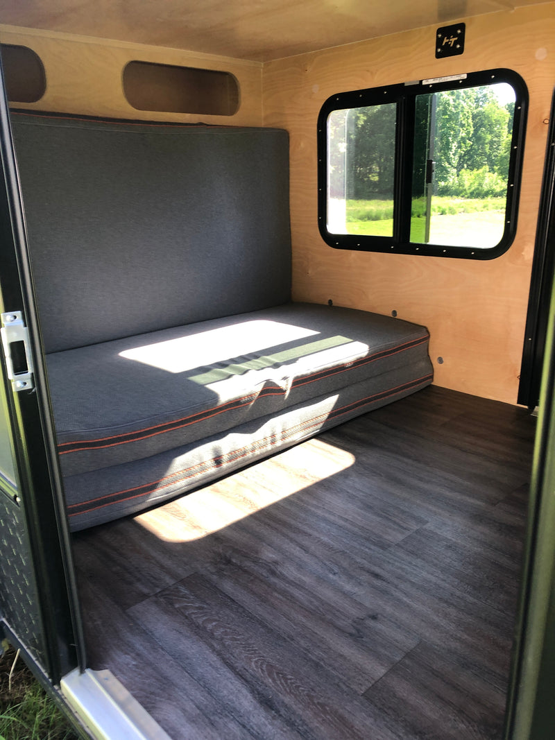 Cozy RV rental camper interior with wooden walls, dark gray seating/bed, wood-look flooring, and a bright window. — photo 5