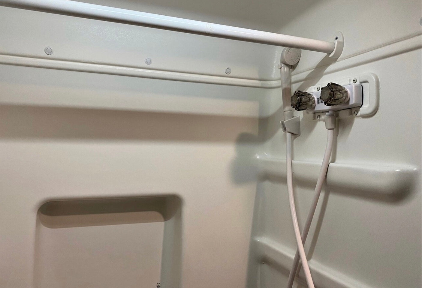 RV rental shower: White molded walls, curtain rod, and basic fixtures with hot/cold handles, showerhead, and hoses visible.