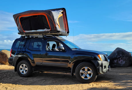 Dark SUV with rooftop tent parked on a sandy beach. Ready for your RV rental adventure by the ocean.
