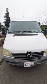 White Mercedes-Benz Sprinter van, a common RV rental choice. Features CA plate, peeling paint, and yellowed headlights.