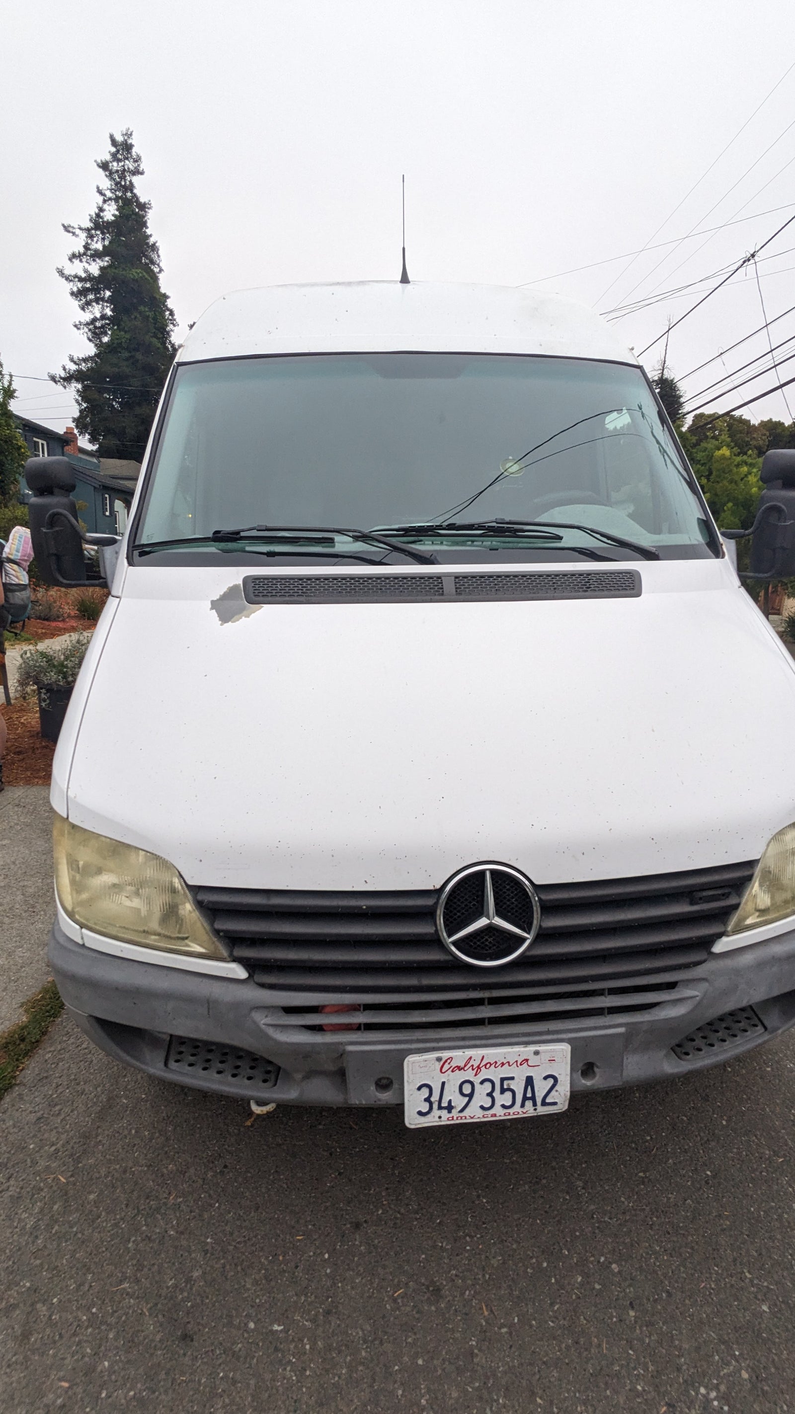 White Mercedes-Benz Sprinter van, a common RV rental choice. Features CA plate, peeling paint, and yellowed headlights.