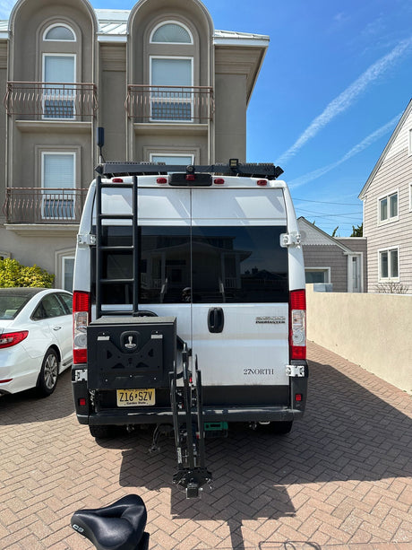 White Ram ProMaster RV rental van equipped with a ladder and bike rack, seen parked on a brick driveway.