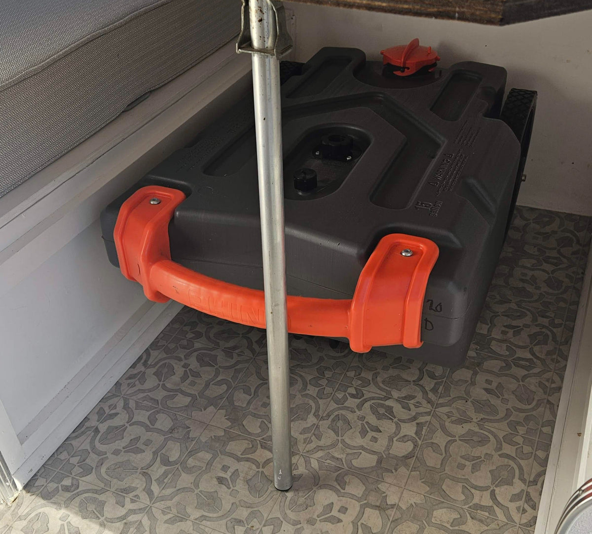 Grey water tank with orange handles stored under a bench in an RV rental, on patterned flooring. — photo 16