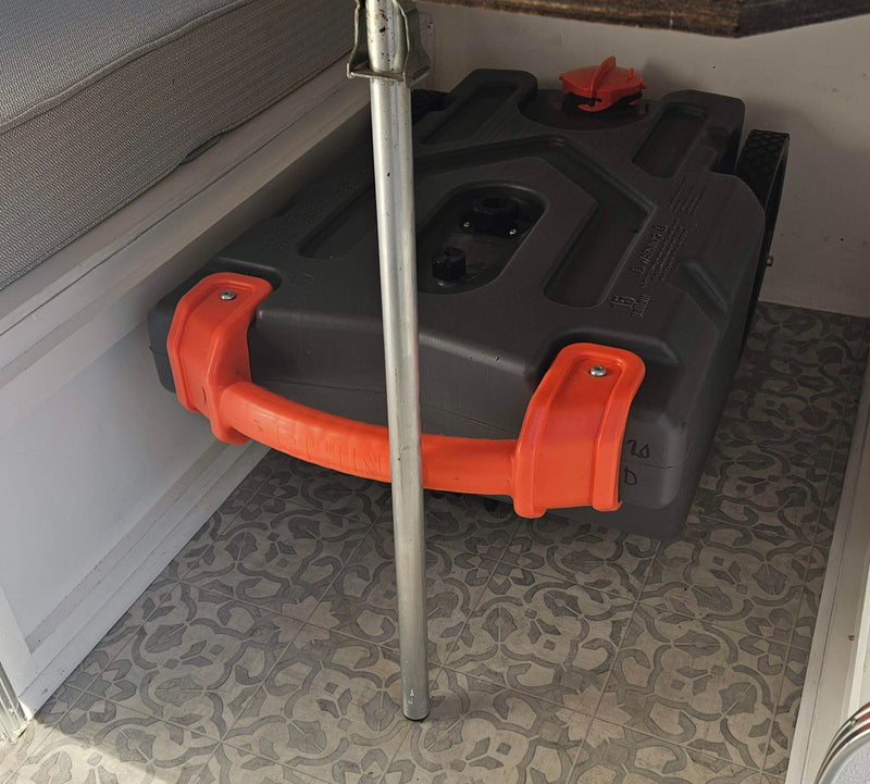 Grey water tank with orange handles stored under a bench in an RV rental, on patterned flooring. — photo 16