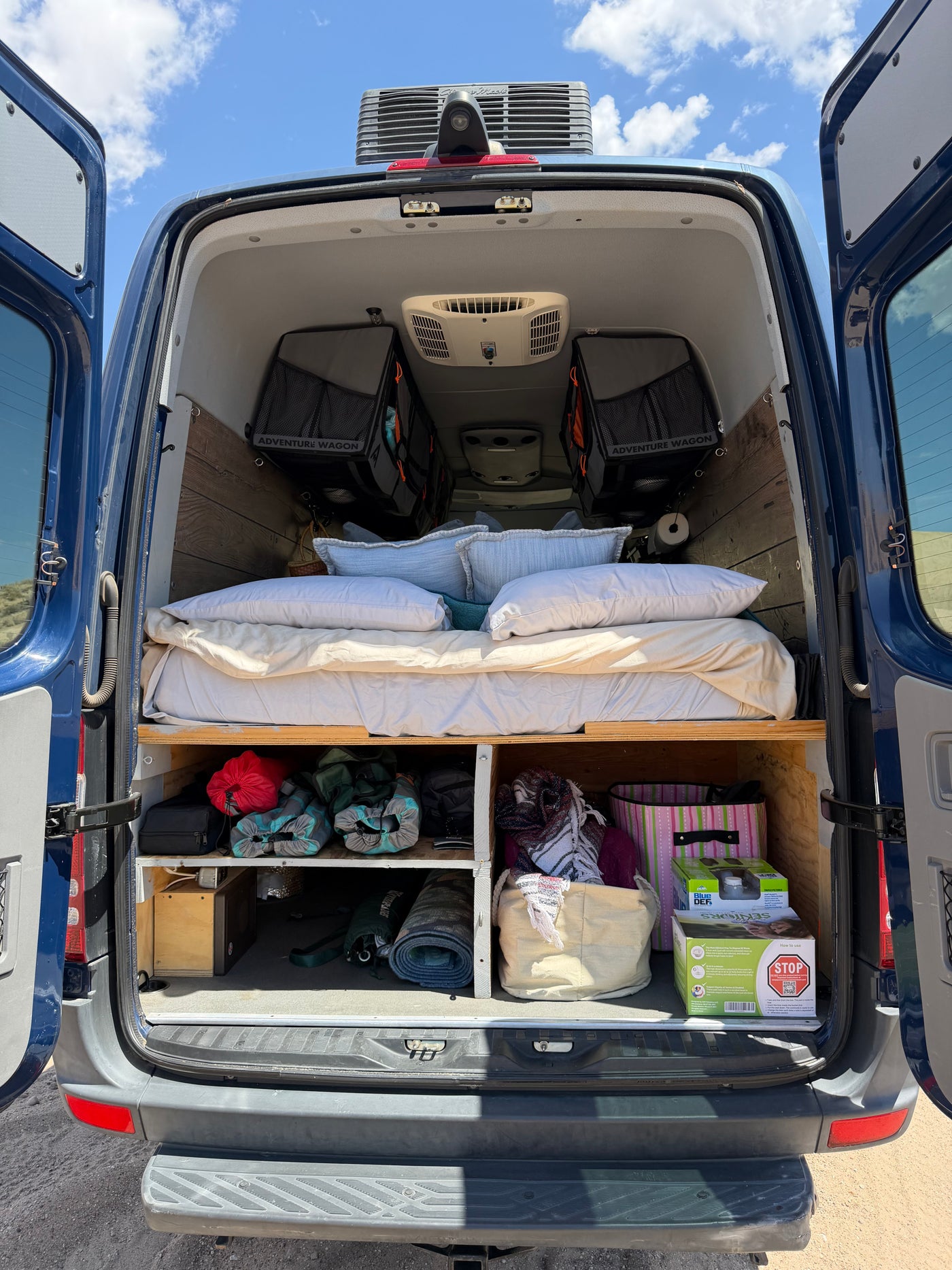 Spacious rv rental camper van interior showing a comfy bed, overhead storage, and gear organized below. — photo 17